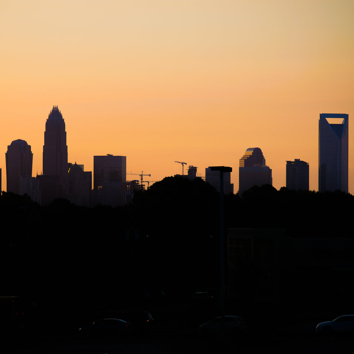 Charlotte, North Carolina skyline silhouetted against a warm orange sunset, featuring the city's iconic Uptown skyscrapers.